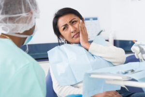 Female patient holding jaw in pain seeking treatment for TMJ in dentist office