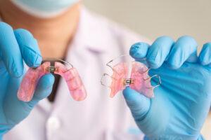 Dentist holding up pink retainers in office