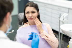 woman holding face in pain before getting tooth extraction in dentist office
